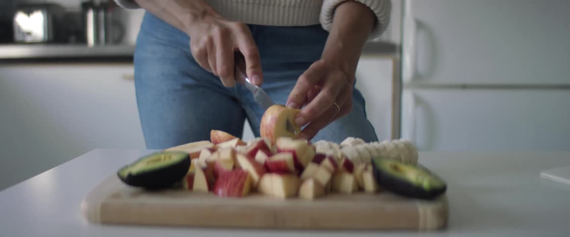 Woman cuts vegetables and fruits with a sharp kitchen knife on a cutting board in the kitchen