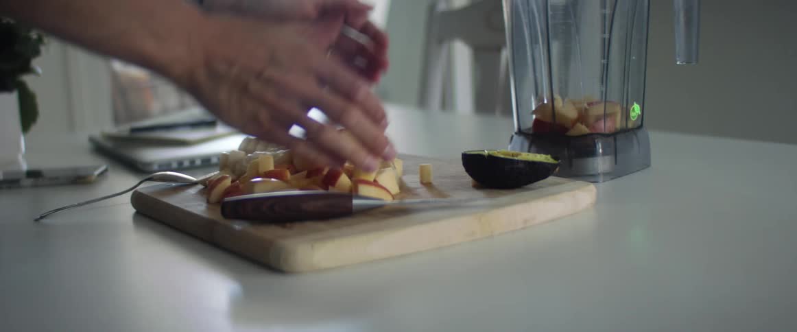 A person scoops cut apples and places them into a blender pitcher