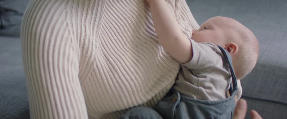 Mother with a white knit sweater breastfeeds her baby