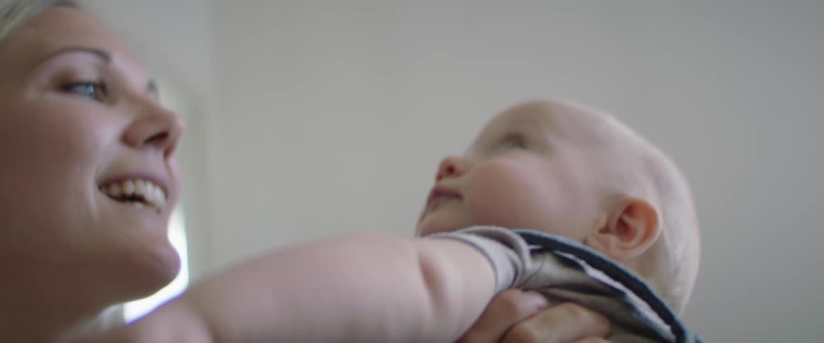 A mother holds her baby son on her lap and talks to him and smiles