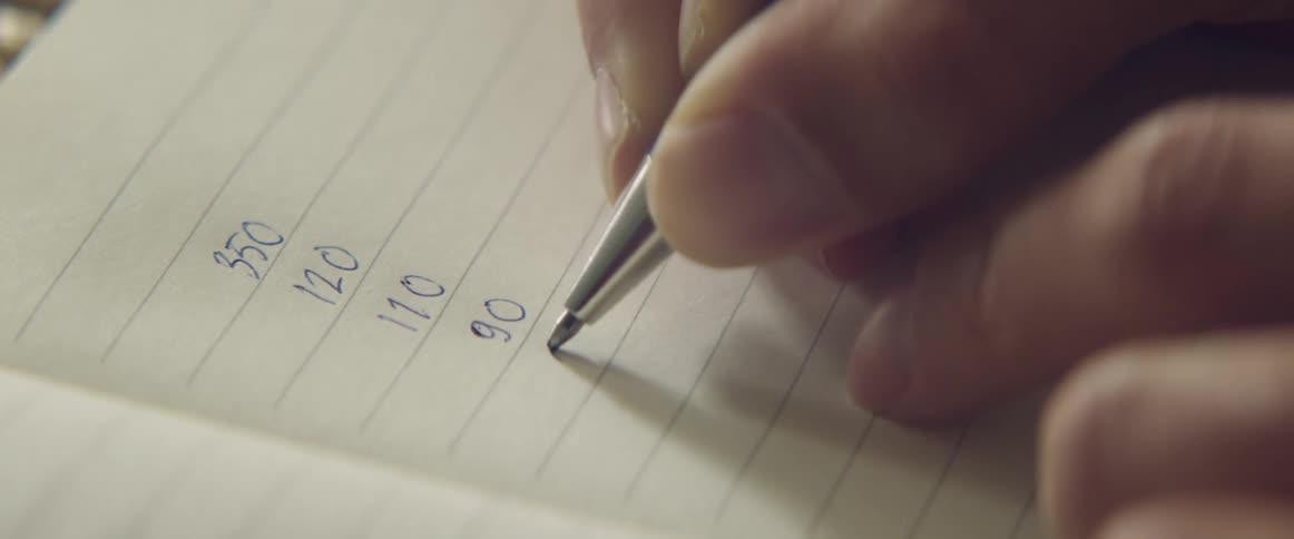 A person writing numbers on paper and adding them up