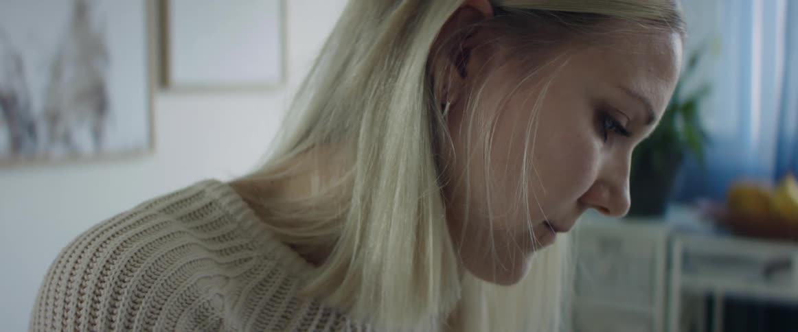Side view of a woman with a white knit sweater and blonde hair looking down in living room