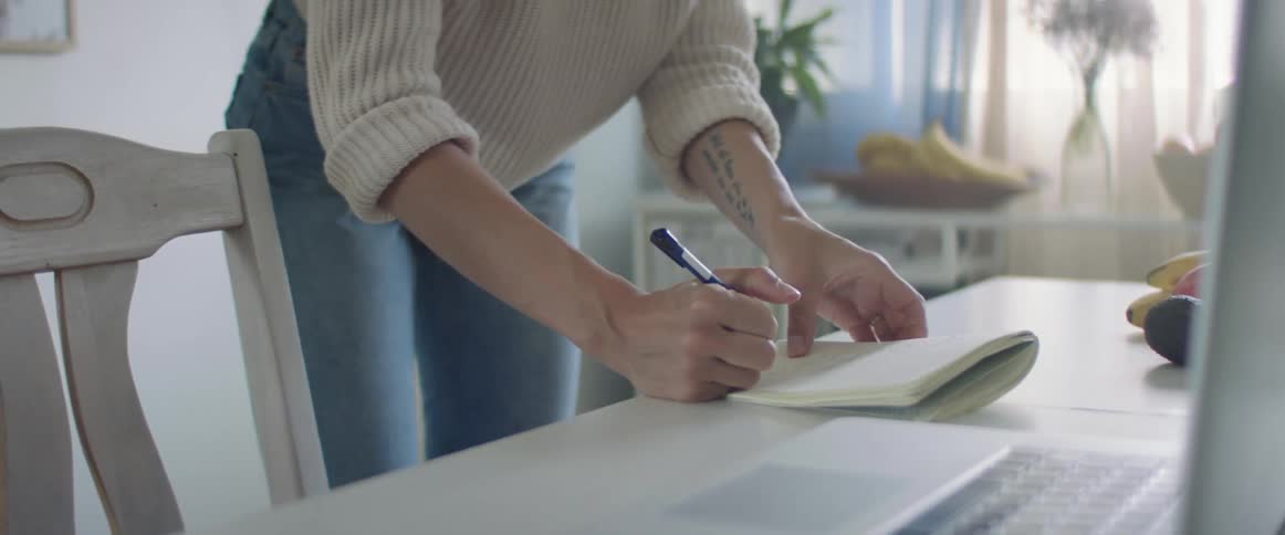 Blonde woman with jeans and a white knit sweater writes things down in a notebook