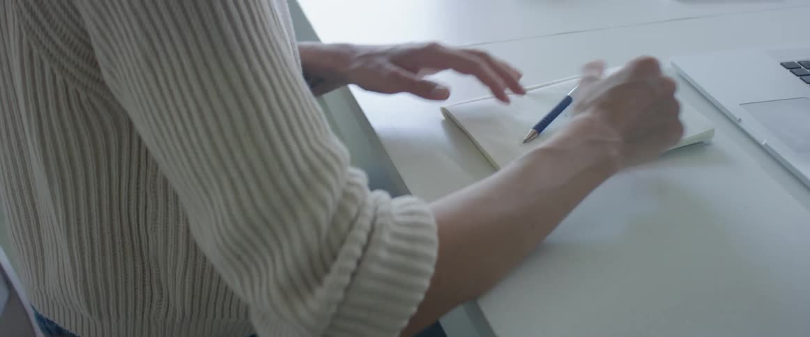 Young woman working at home writes with a pen on a notebook and then types on a laptop