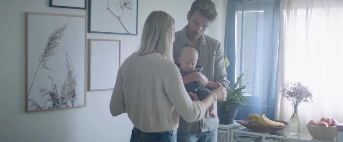 A man holds a baby beside a woman and she turns to play with the baby