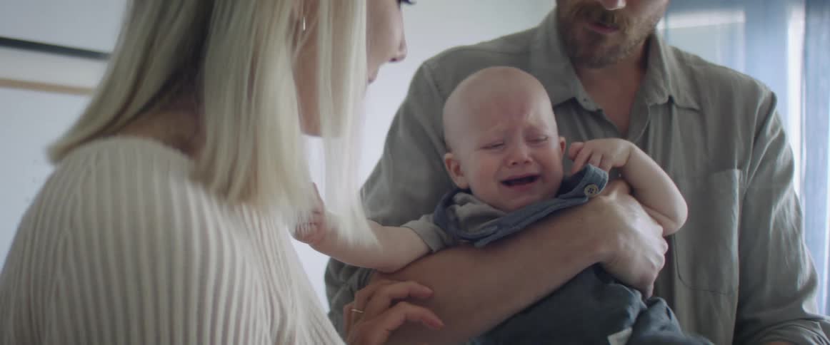 Father hold crying baby next to the mother at home
