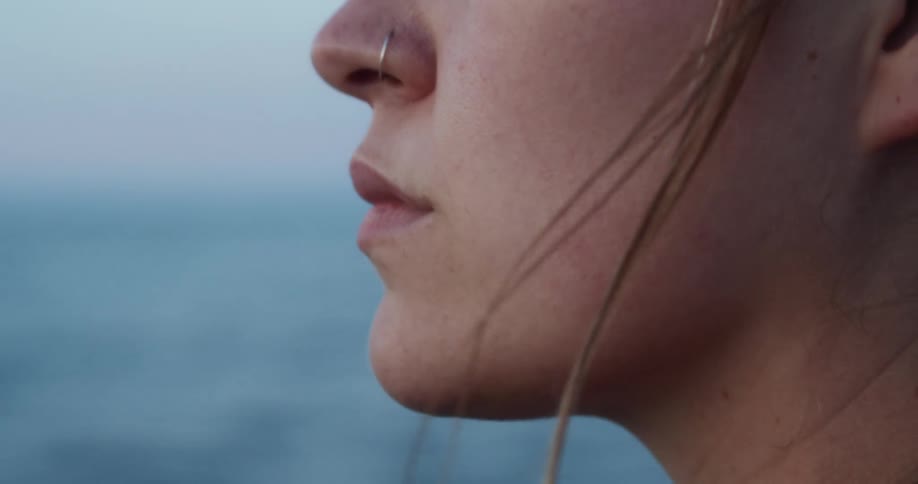 A woman with a nose piercing looks out upon the ocean on an overcast day