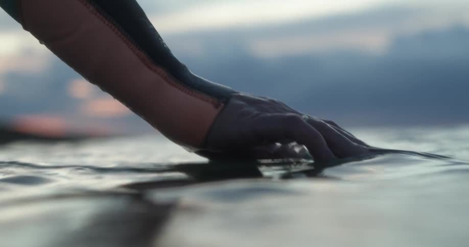 A woman wearing a wet suit and gloves dips both her hands into the surface of the ocean