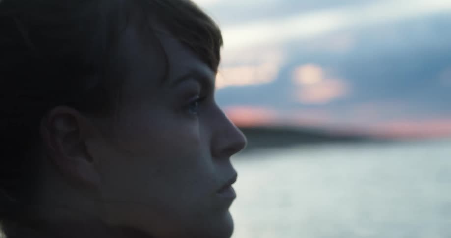 A woman stands outside looking at the ocean and the sky