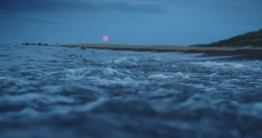Waves of water on the beach with the sun set the sky and clouds in the background