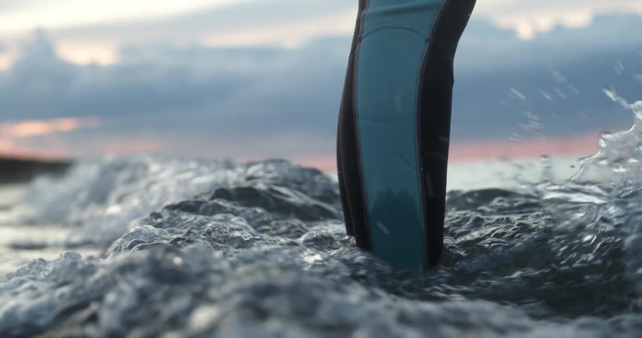 A person stands in the ocean as waves pass over their ankles