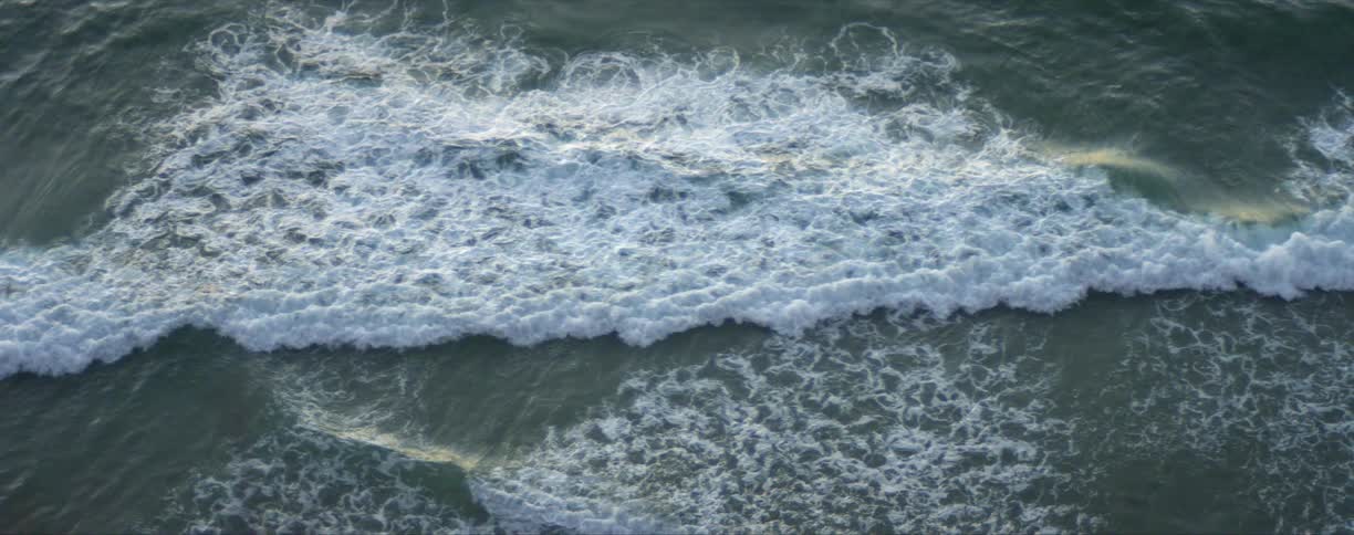 Top down view of sea waves gently crashing on the coast at sunset