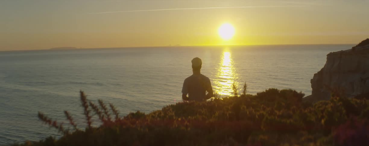 A silhouetted man watching a sunrise over ocean water