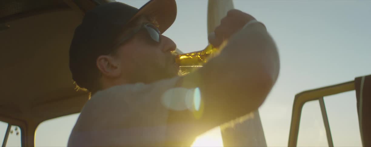 A man stands next to his vehicle and drinks a beer