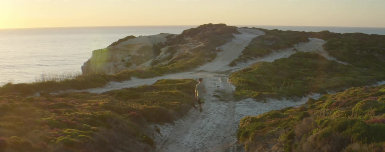 A man walking down a trail near an ocean