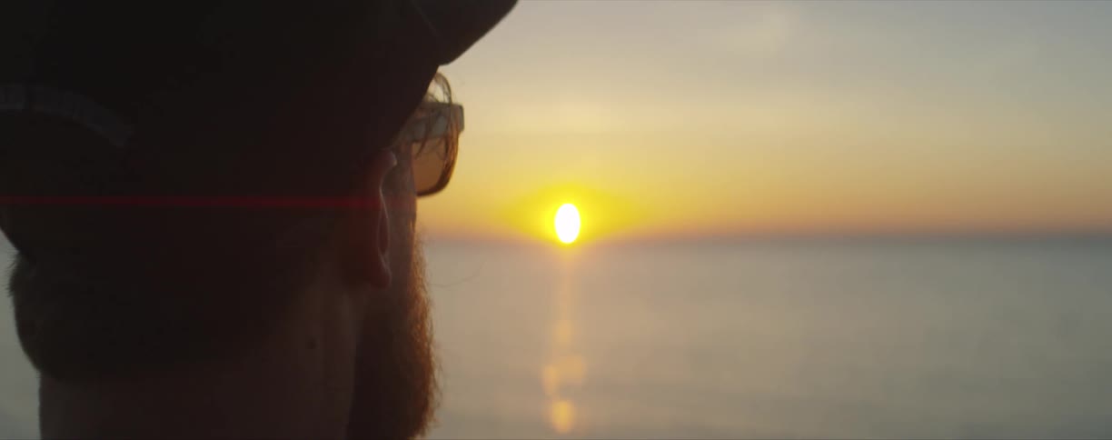 A man looks at the sun setting over a lake