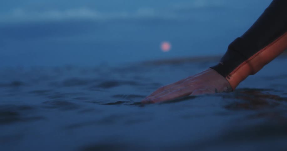 Red moon hanging over the ocean water where a man in a wetsuit floats