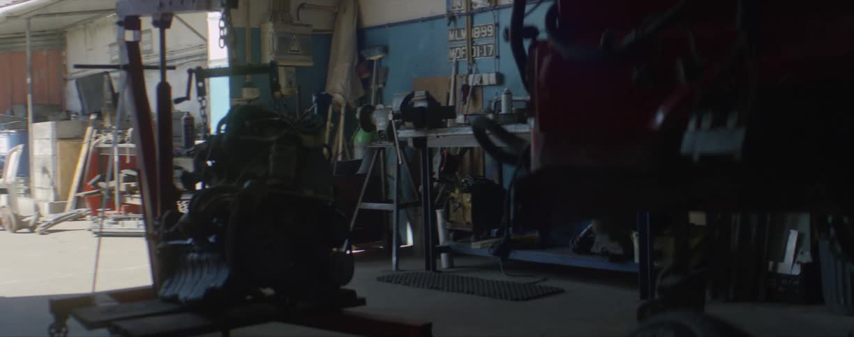 Large piece of equipment on a small engine crane and sitting on a platform in a large open garage with other equipment nearby