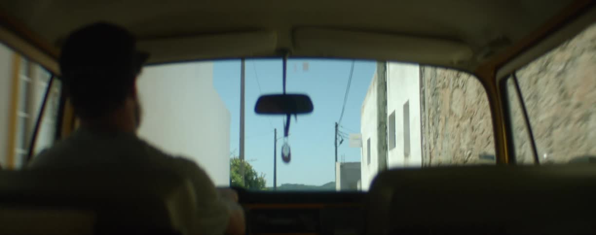 A man drives a vehicle through a narrow alley between buildings on a sunny day