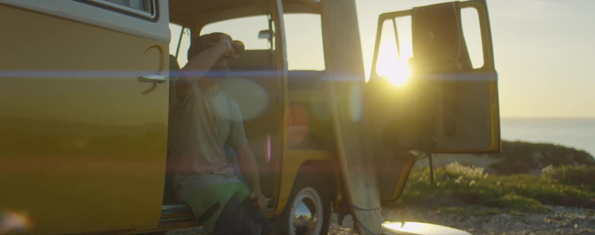 Man sitting on a bright yellow van drinking beer near the beach at sunset