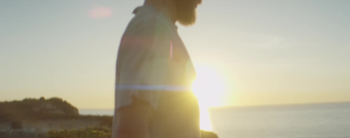 A man walks along the shore as the sun sets over the water