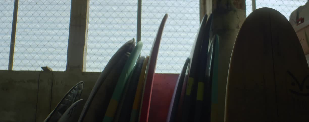 Colorful surfboards piled up against the wall inside a dimly lit storage room