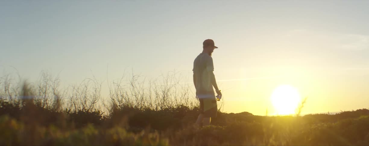 A silhouetted man walking in a field at sunset