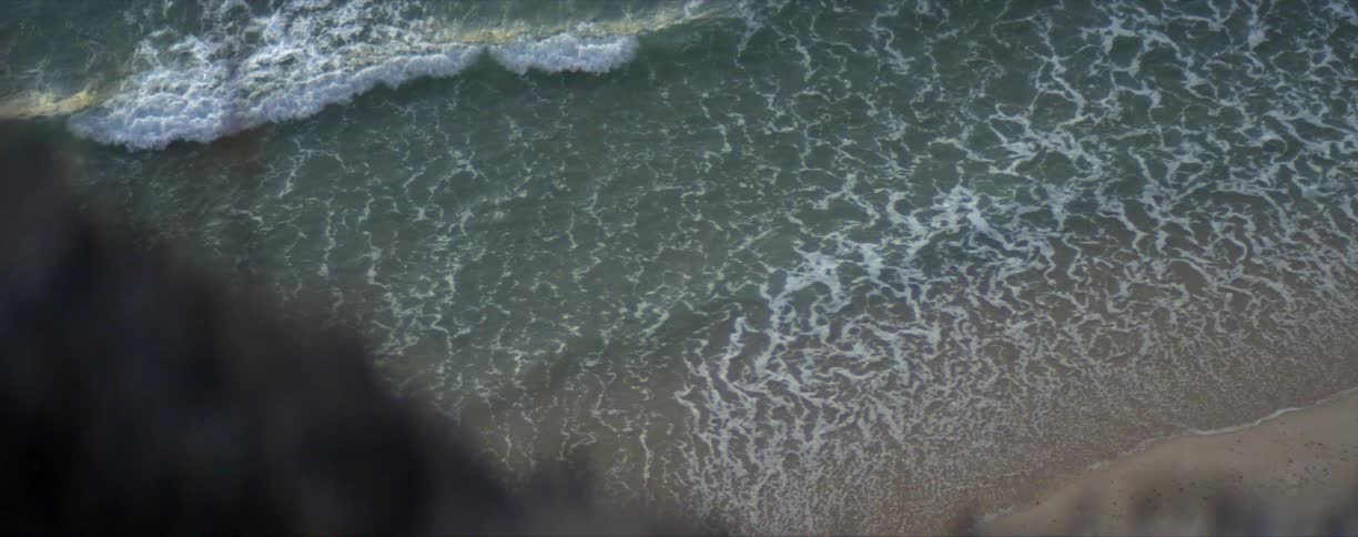 A cliff looking down ocean waves washing into a sandy beach during the day