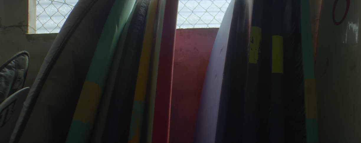Colorful surfboards stacked against a wall near a window inside a dimly lit room