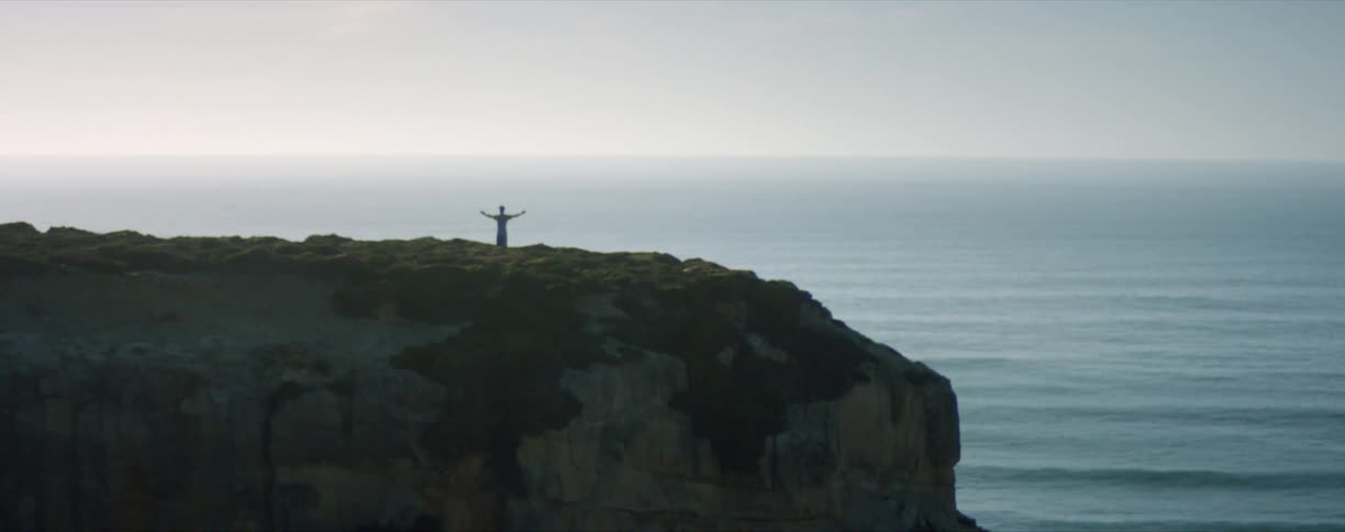 A man standing near a cliff with his hands in the air
