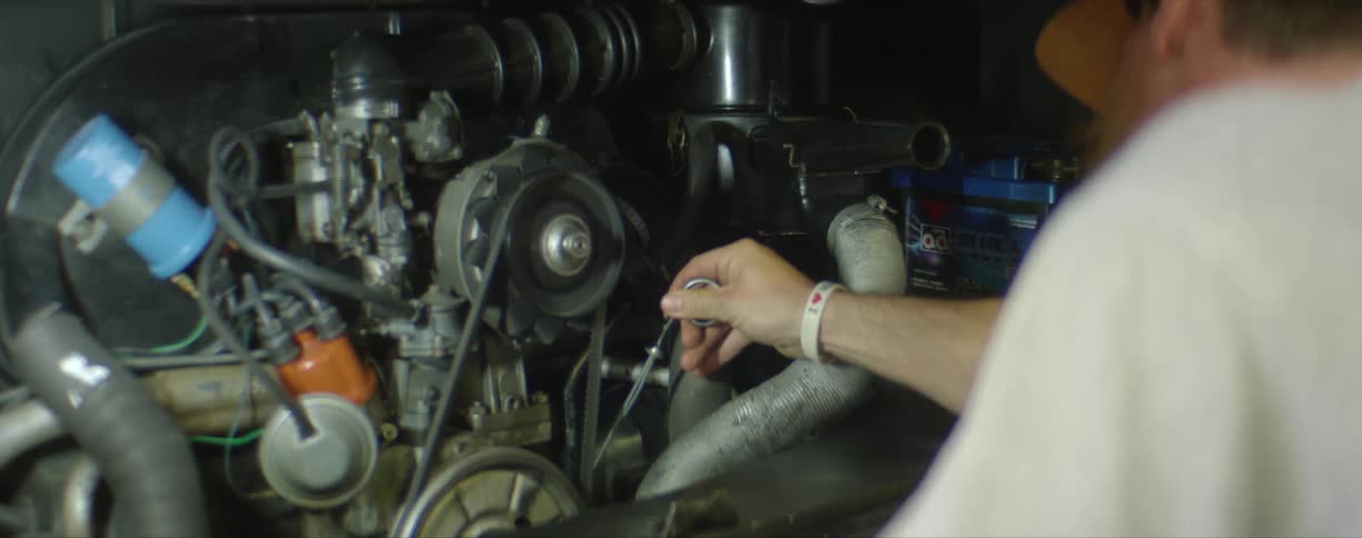 A bearded man wipe a oil dipstick before placing it back into a motorcycle engine