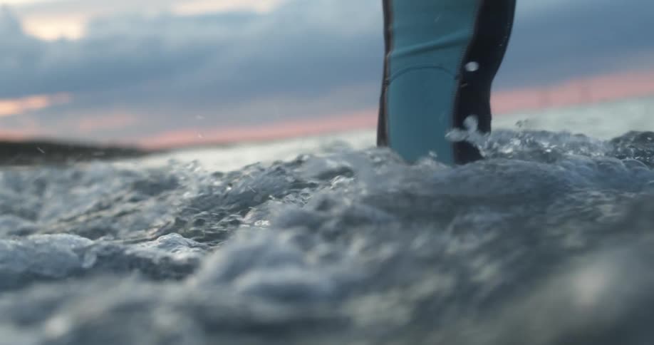 Person standing on a shoreline while the tide flows in up to their knees at sunset