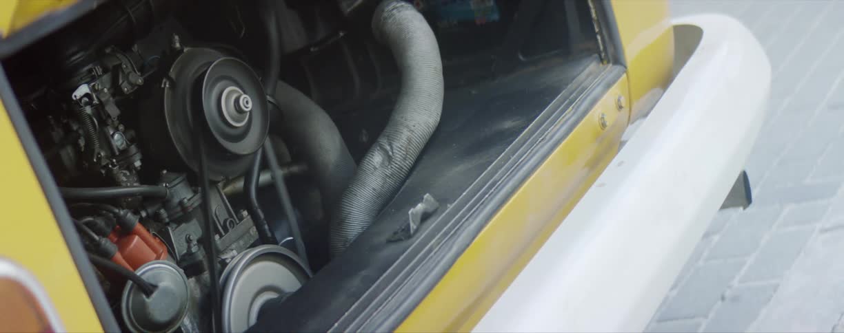 Hood of a bright yellow volkswagen van open showing the engine revving up