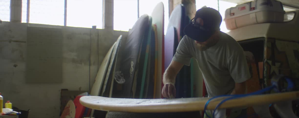 Surfer working with a surfboard inside of a surf shop on a sunny day
