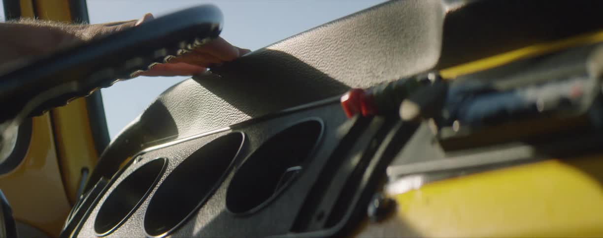 The sun shines onto the yellow dashboard and hands on a steering wheel