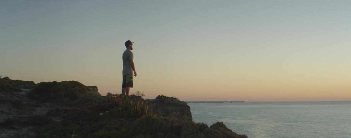 A man stands on the shore and looks out at the water
