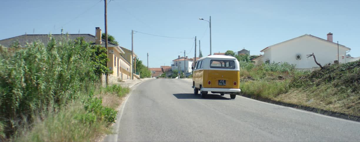 A white and yellow bus drives on a rural road approaching a town
