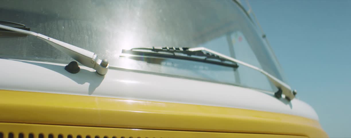 A vehicle windshield with windshield wipers with the sky and clouds in the background