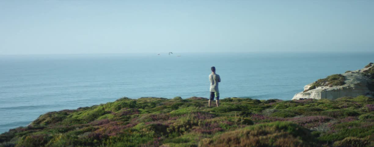 A man stands outdoors overlooking the ocean