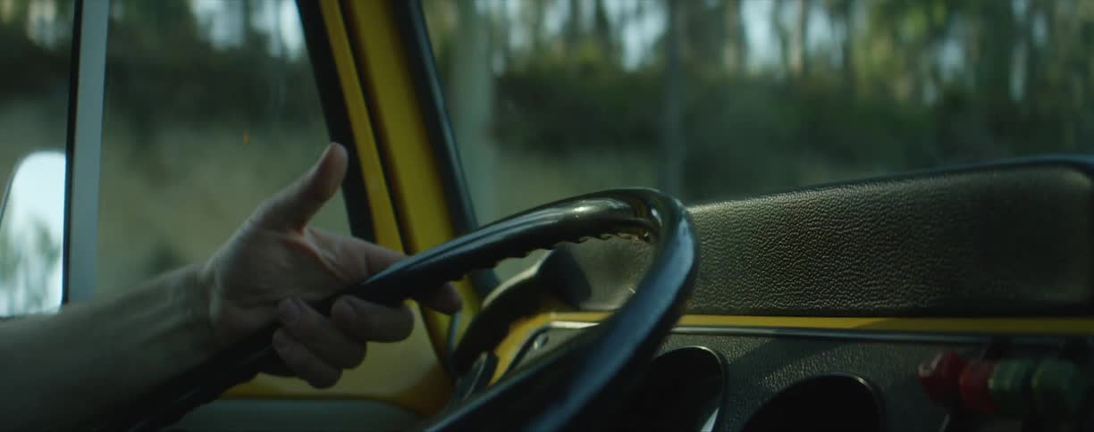 A mans hand on a steering wheel while driving by trees on a rural road