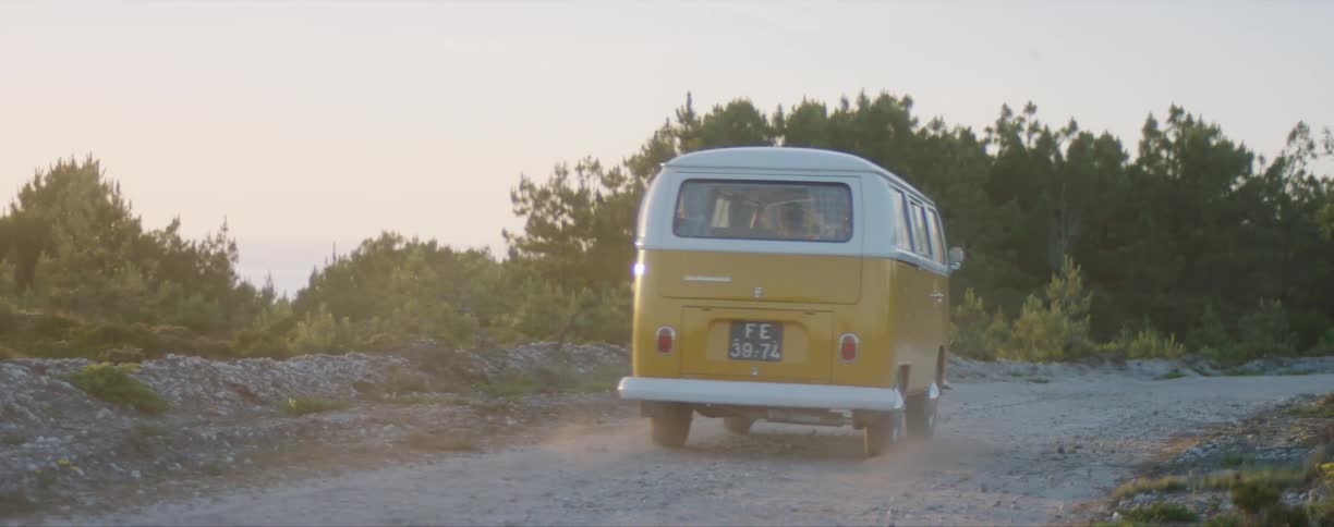 Yellow and white wagon van drives down a dirt road next to bushes at daytime