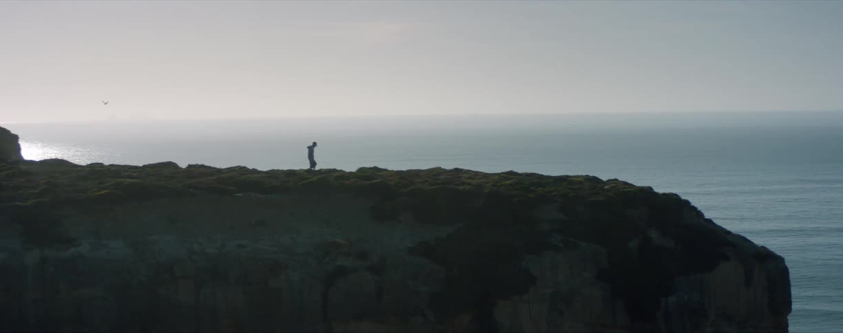 Silhouette of a young man standing over the edge of a cliff near the ocean