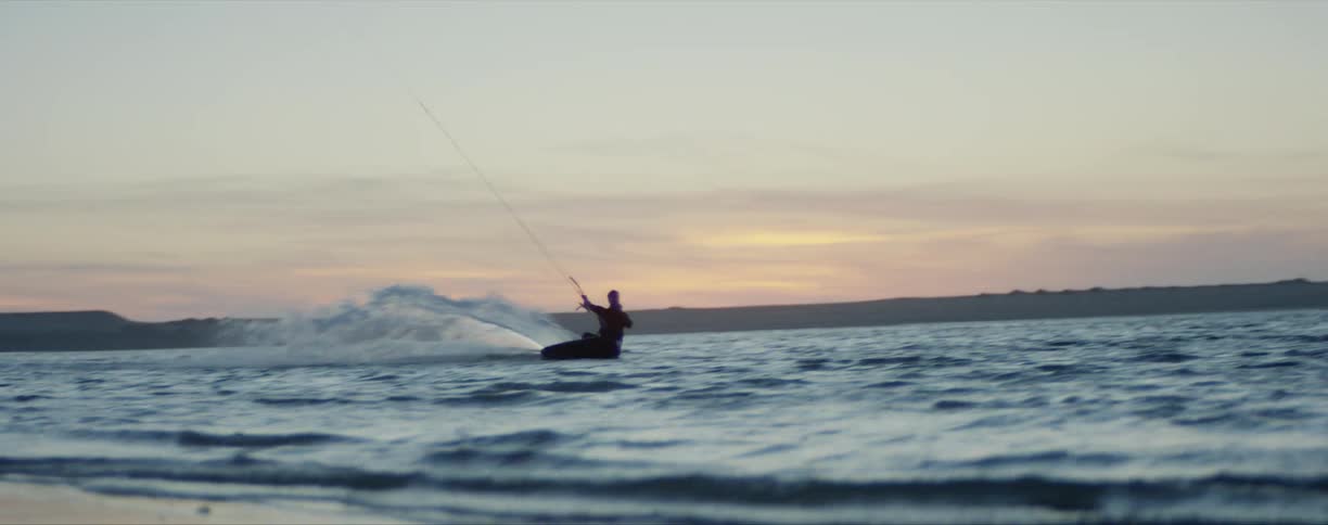 Man kite surfing on the ocean near the coast at sunset