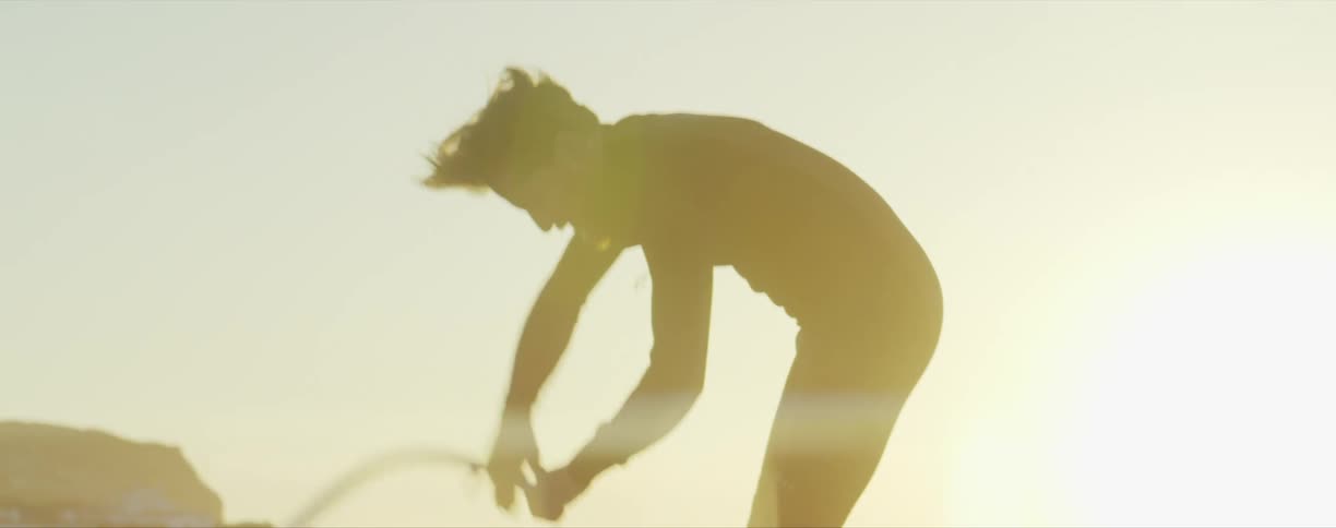 A man in a wet suit picks up an airpump and attaches a hose while the ocean breeze blows