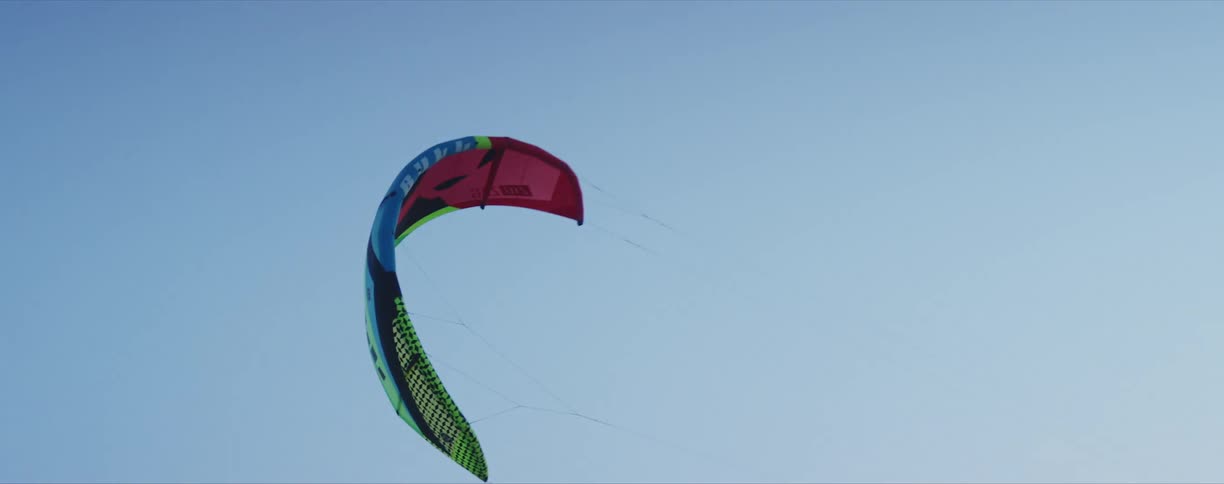 A parachute kite with wires in the air against a blue sky