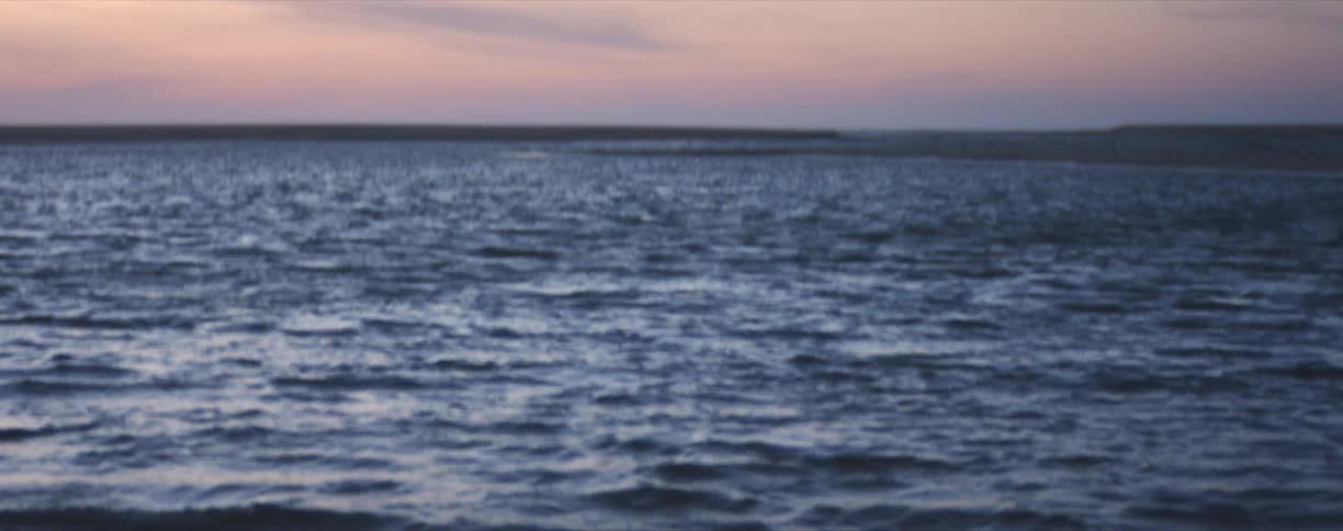 Gentle waves lapping at shoreline revealing a wake boarder at sunset