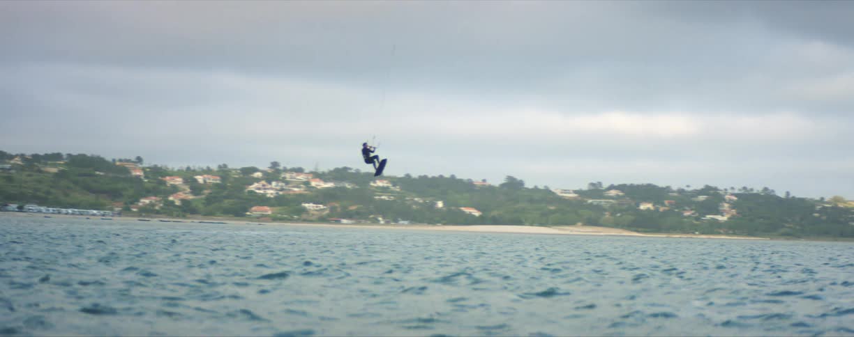 A person kite surfing in a body of water with land the sky and clouds in the background