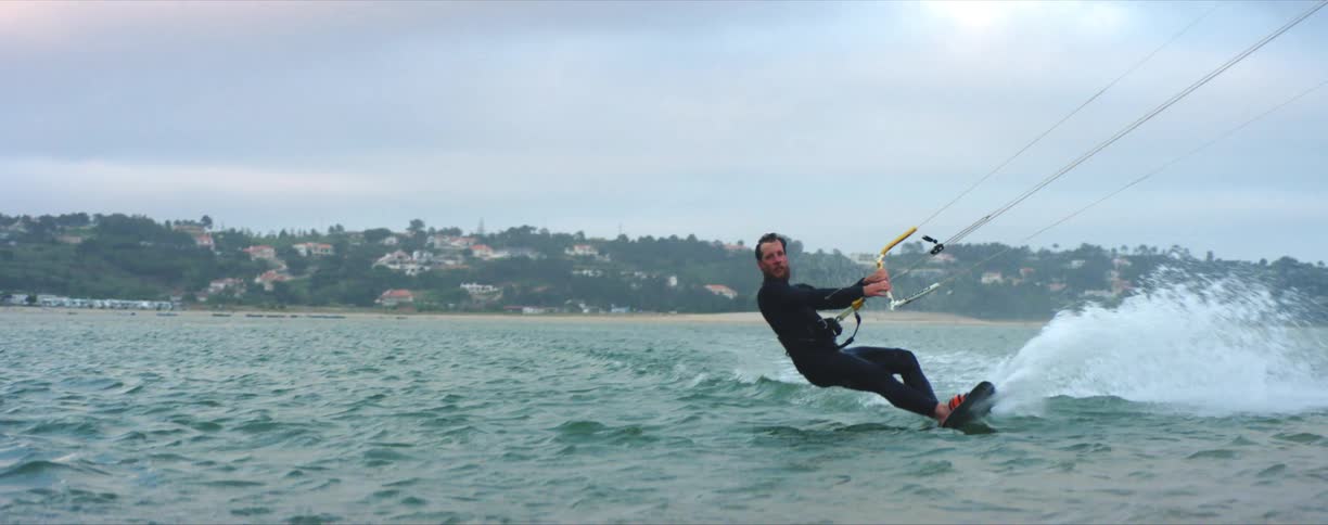 Young bearded man wearing black wet suit kite surfing near the coast