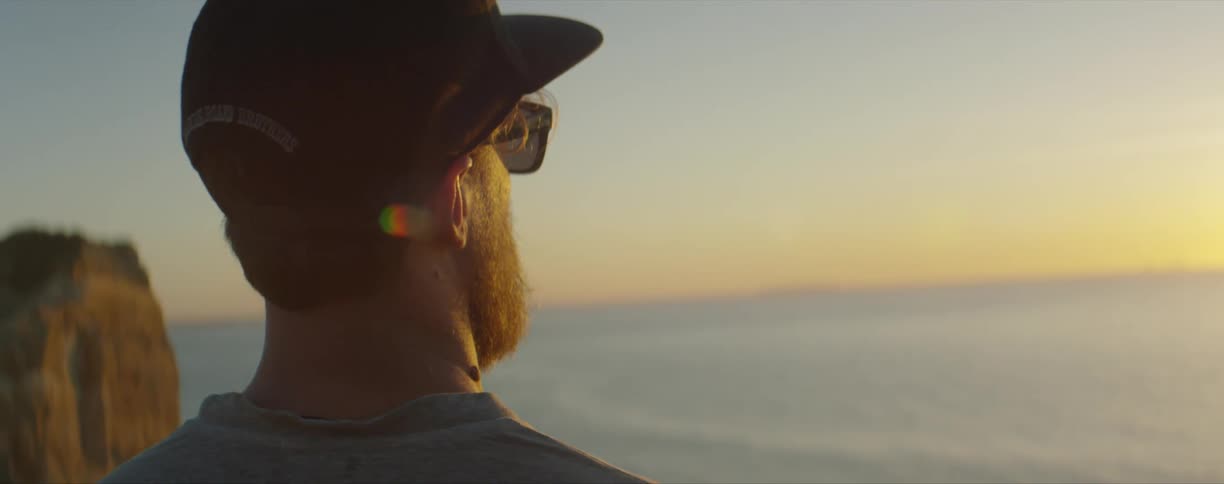 Man wearing sunglasses looking at the sun setting over the ocean at sunset