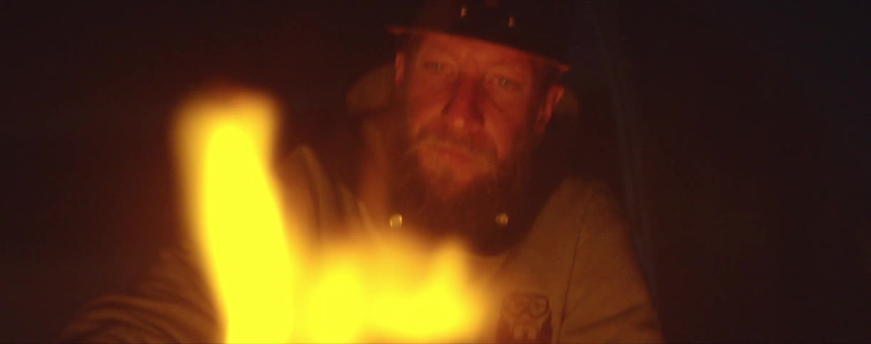 A man sits in front of a fire outside